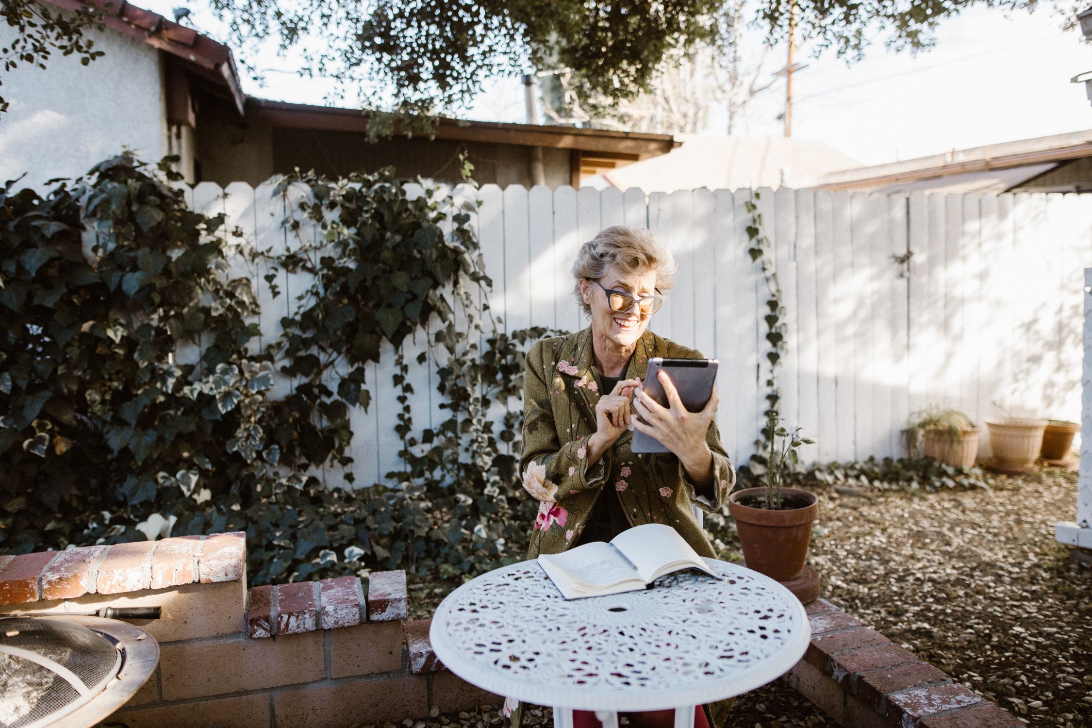 Smiling older woman with glasses using a tablet in a sunny backyard garden