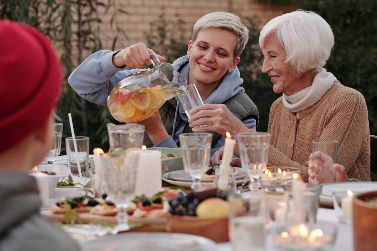 Younger woman pouring a drink for an older woman at a candlelit outdoor family dinner