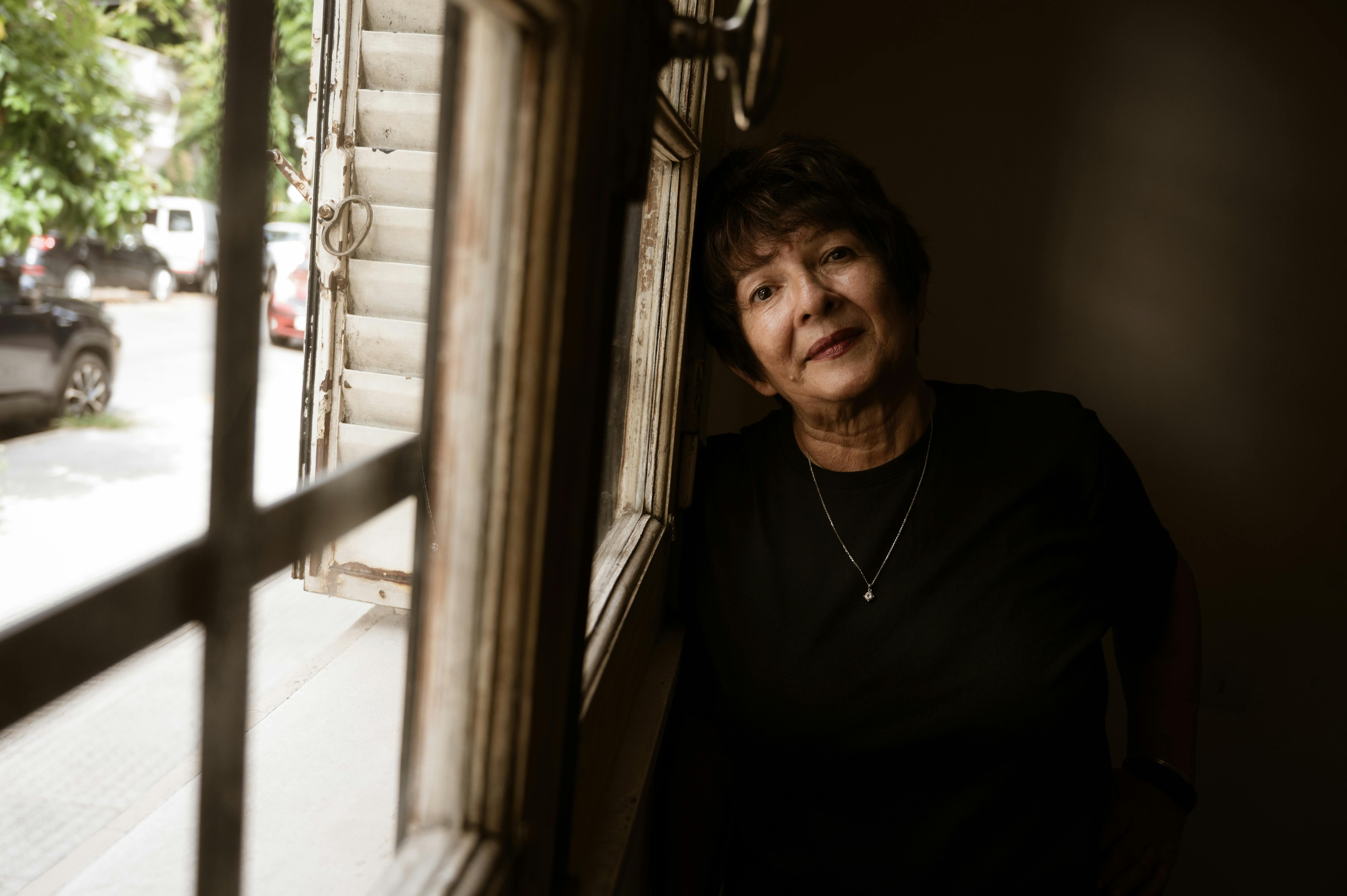 Older woman leaning by an open window, looking outside
