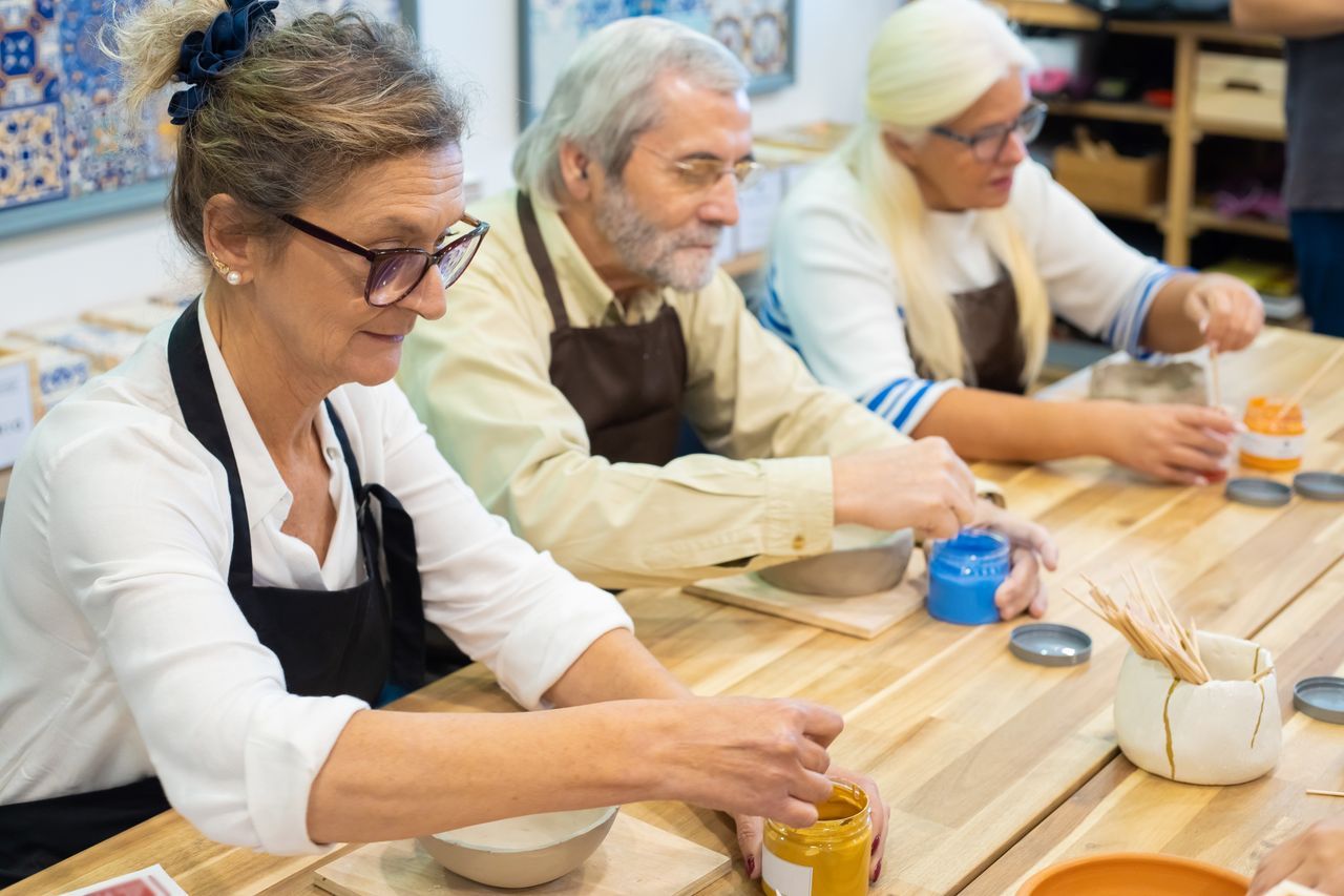 Adults painting ceramic pieces together at a pottery workshop table
