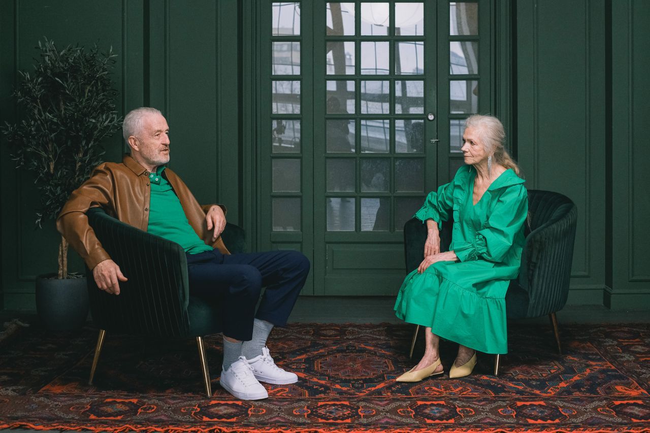 Older man and woman seated in separate armchairs facing each other in a green-paneled room