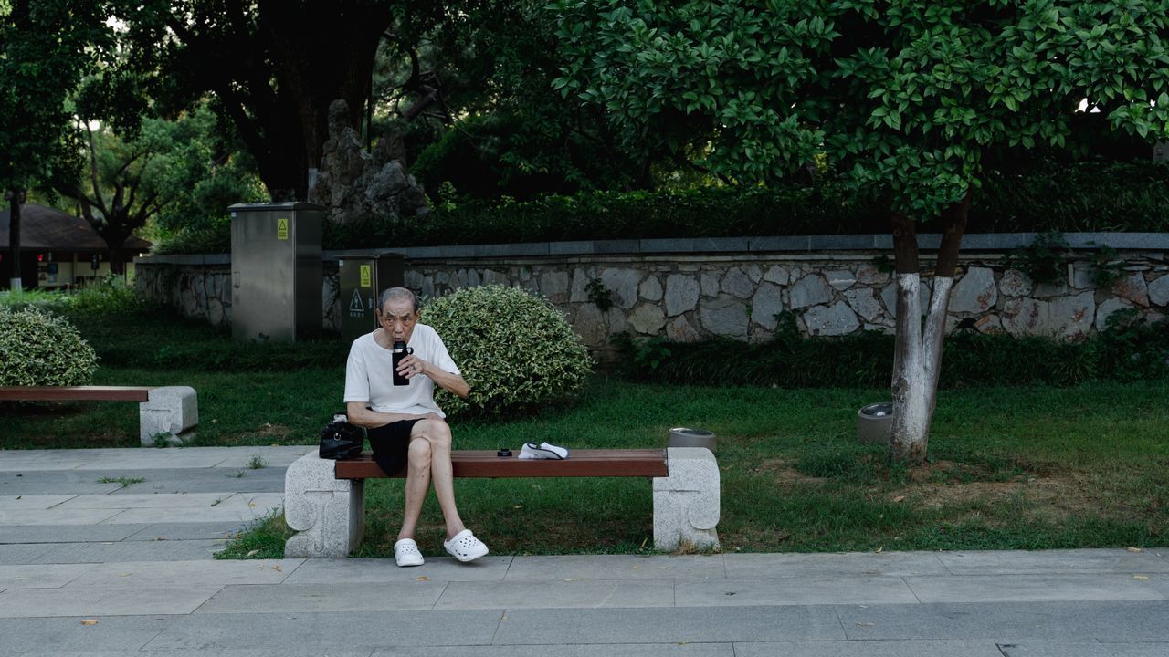 Older man sitting alone on a park bench looking at his phone