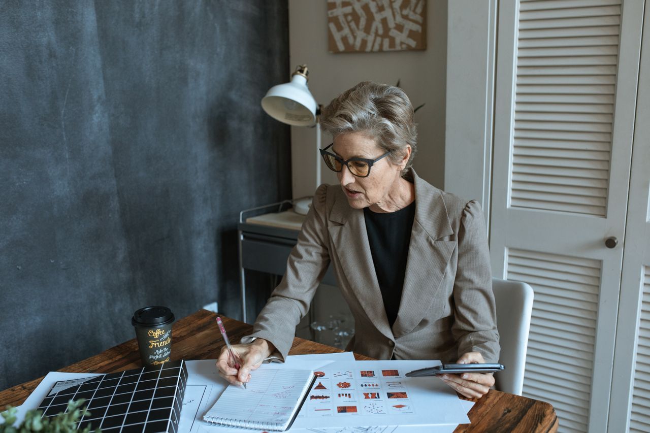 Senior woman in eyeglasses taking notes at a table with documents and coffee