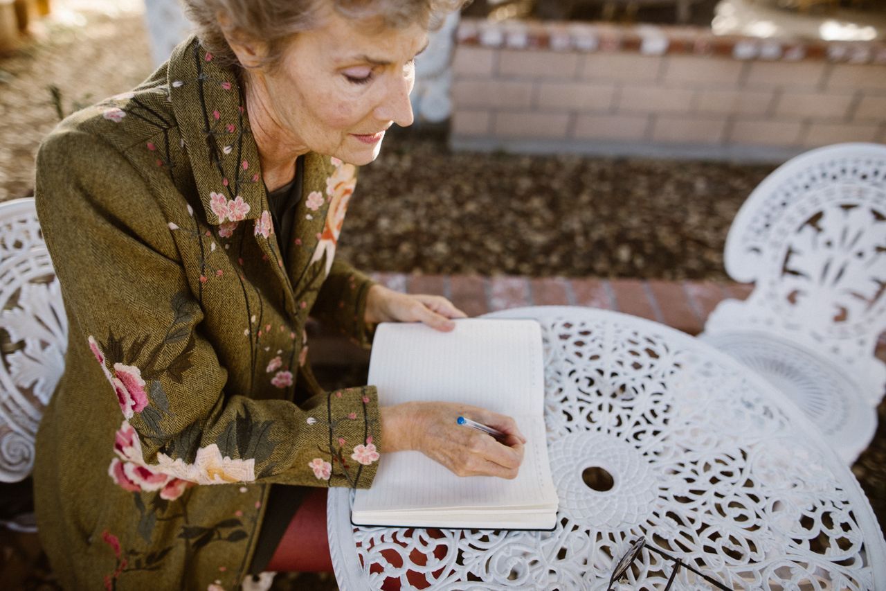 Senior woman writing in a notebook outdoors in a peaceful garden setting
