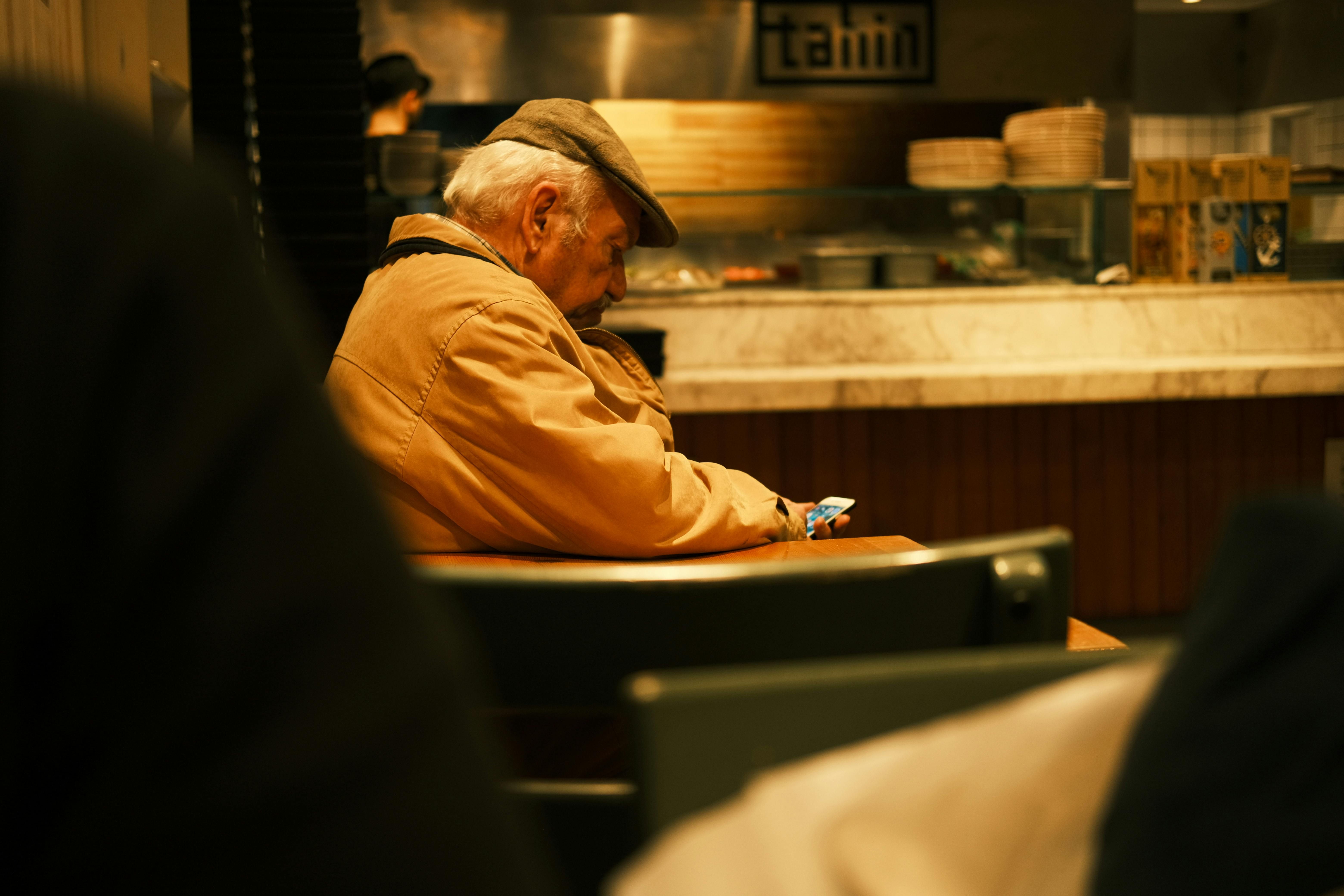 Older man looking at his phone while sitting alone in a warm cafe