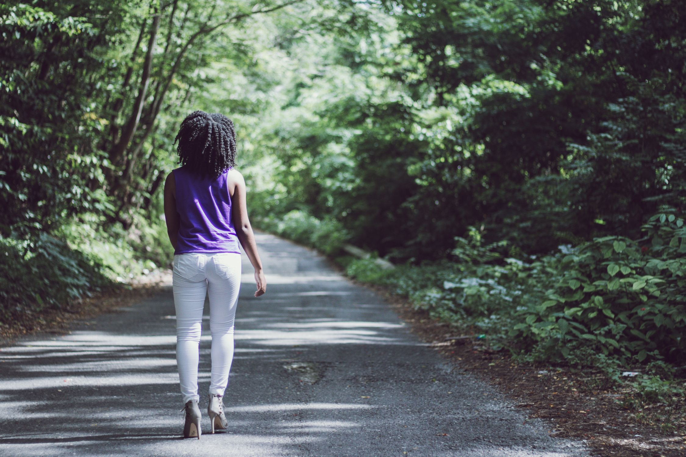 Woman over 50 walking alone through a sunlit botanical garden path