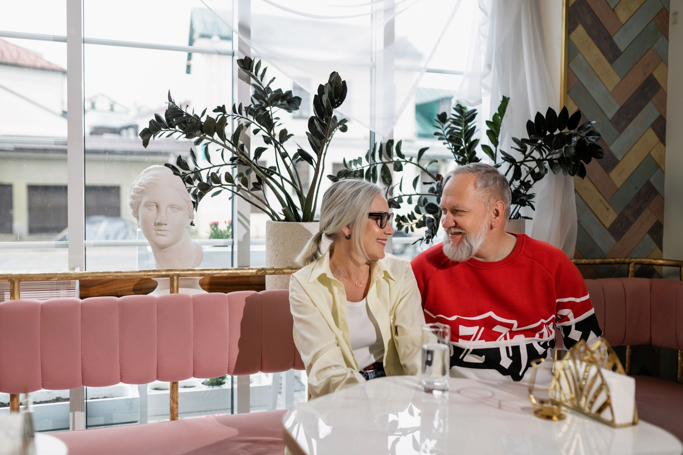 Couple over 50 leaning toward each other in warm conversation at a cafe table