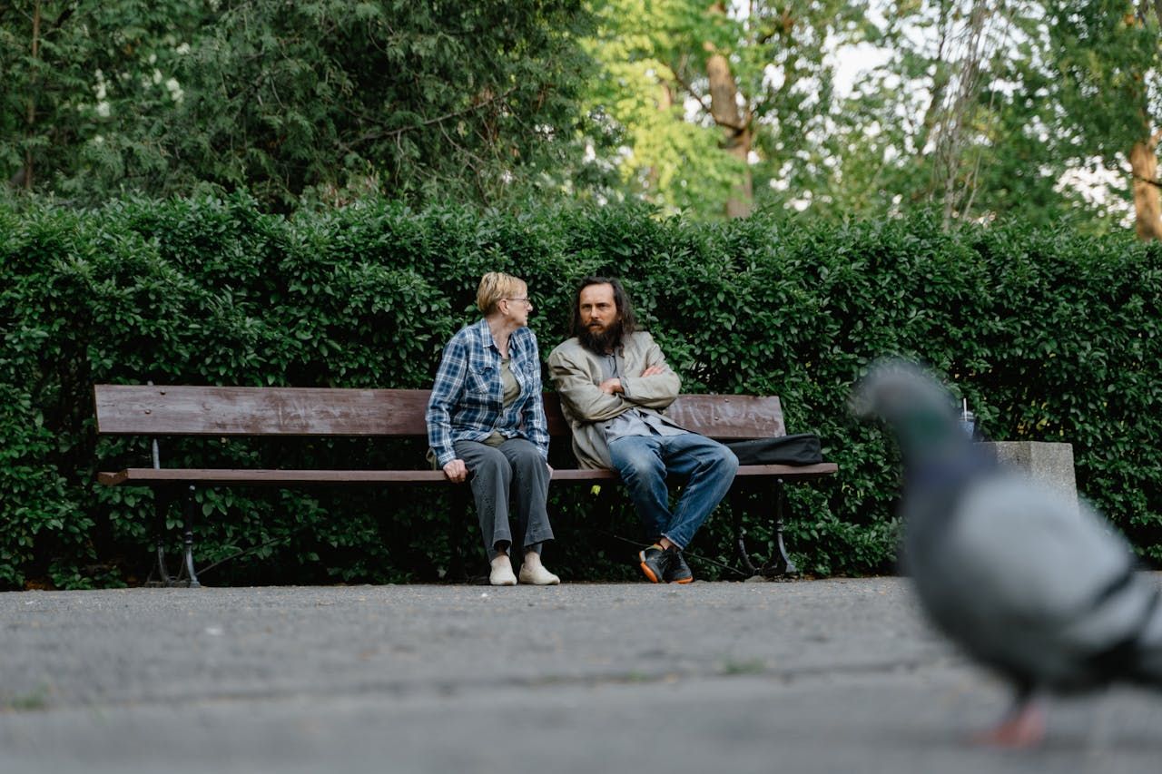 Older man and woman sitting on a wooden park bench having a conversation