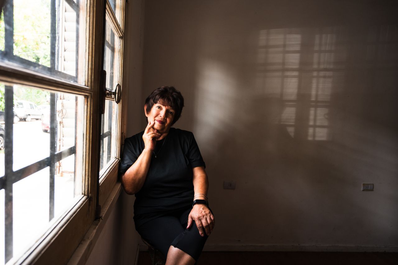 Woman over 50 sitting alone by a window in soft light looking thoughtful