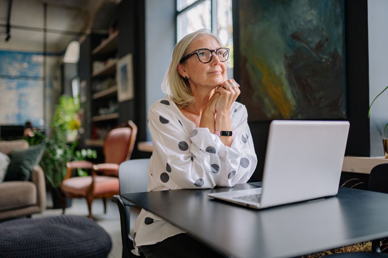 Woman with grey hair and glasses pausing thoughtfully at a modern home desk
