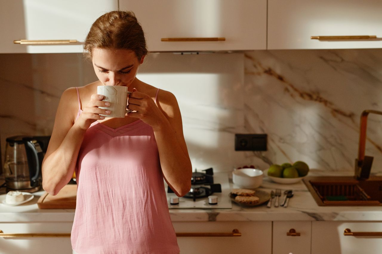 Woman over 50 enjoying a hot drink in a sunlit kitchen in the morning