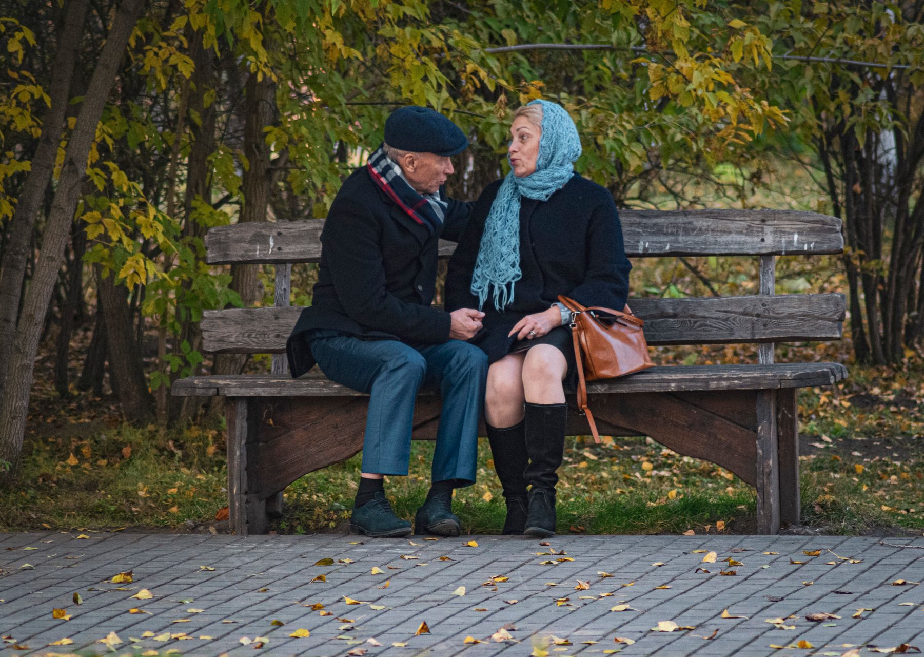 Senior couple sitting close together on a park bench surrounded by autumn leaves