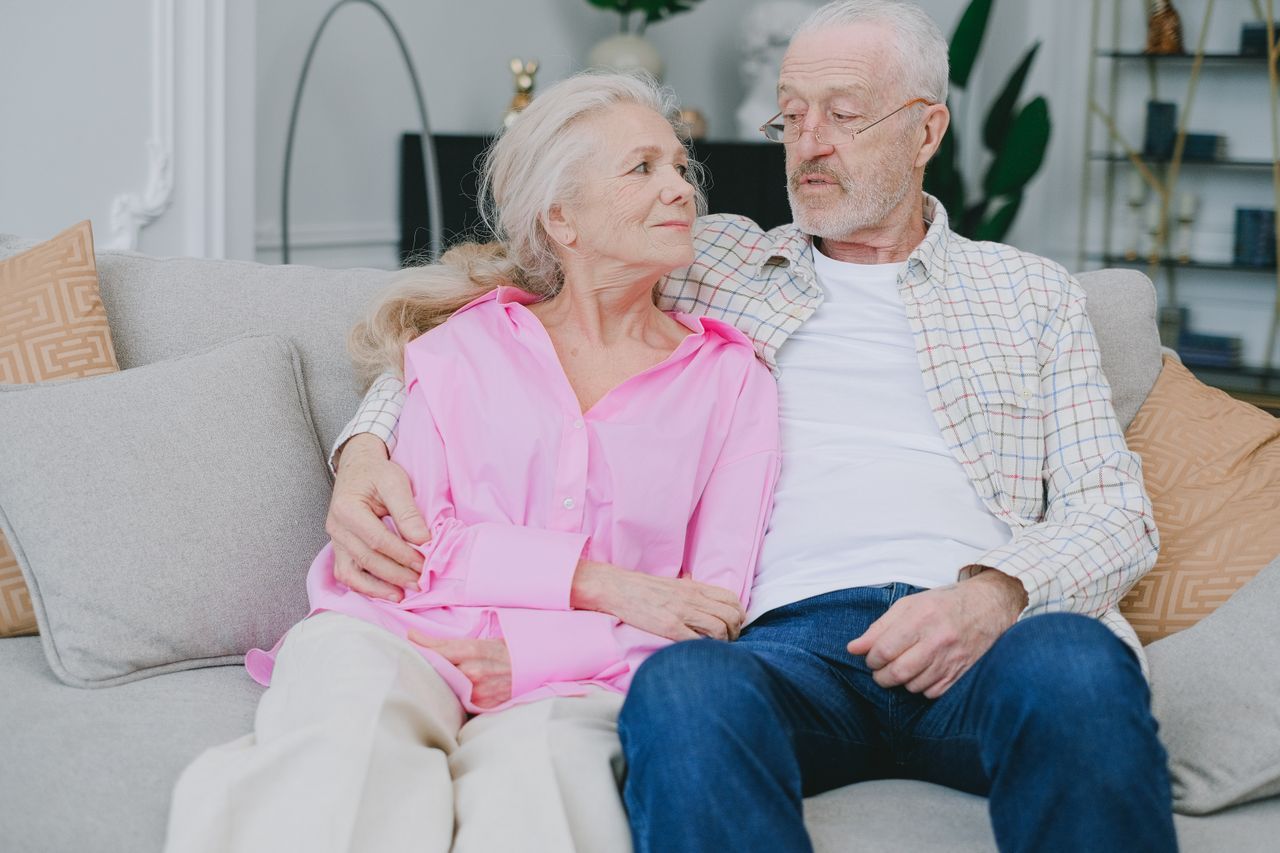 Couple over 50 holding hands on a sunlit park bench in quiet closeness