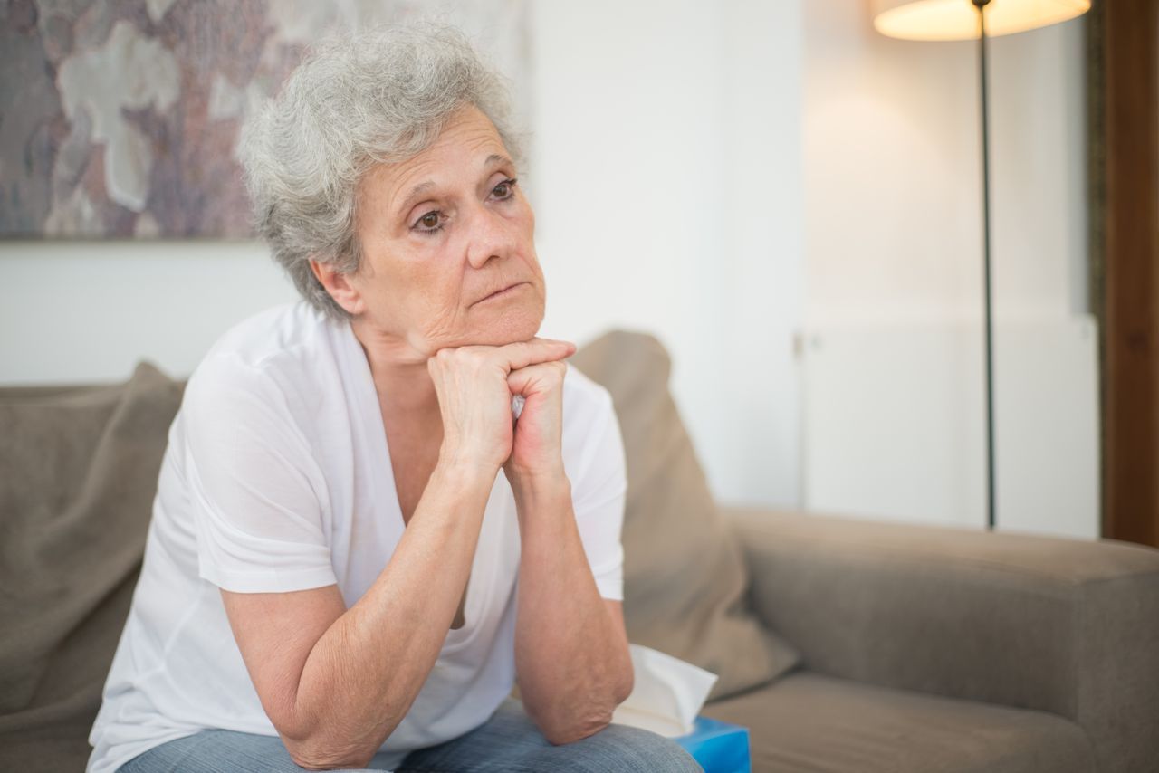 Grey-haired woman sitting indoors with a reflective expression