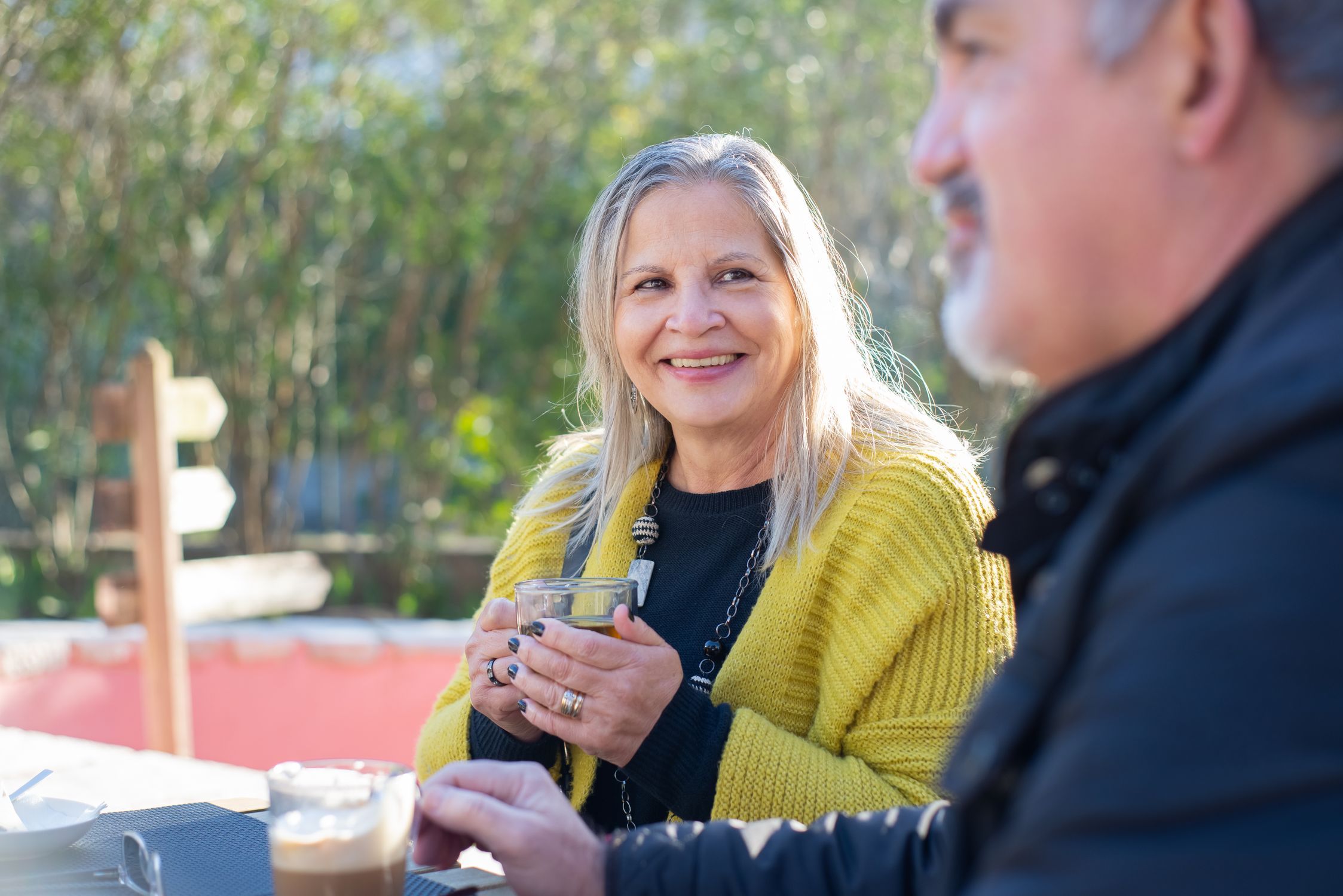 Two people over 50 talking at a small cafe table in warm afternoon light