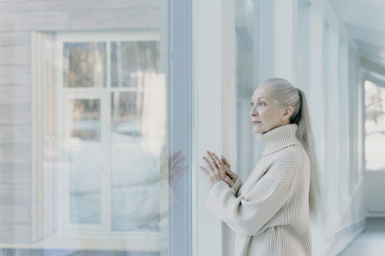 Older woman looking out a window with soft morning light on her face