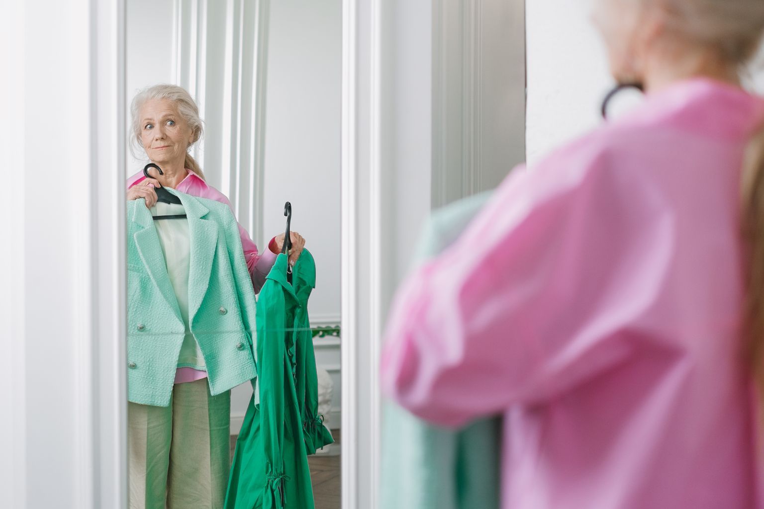 Older woman comparing two outfits in front of a dressing room mirror