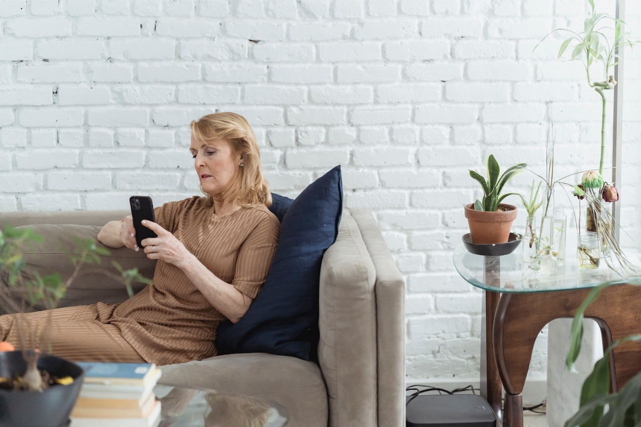 Woman over 50 sitting on a sofa looking at her phone with a calm expression